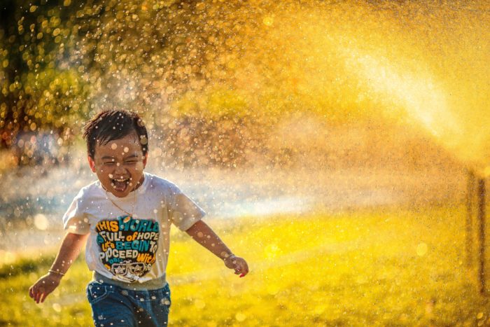 Enfant riant et courant sous un jet d'eau lors d'une sortie en extérieur